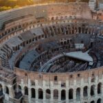 Veduta aerea panoramica del Colosseo a Roma durante il tramonto con i fori imperiali sullo sfondo.